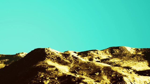 Mountains rise against a bright sky. The ground has rocky surfaces with various textures and colors. Shadows and light create depth on the mountain slopes.