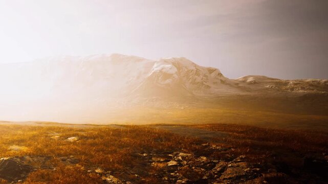 A valley lies below distant mountains, covered in mist with a warm glow from the setting sun. Rocky terrain is visible, showing patches of grass and moss. Light fog lingers in the air.