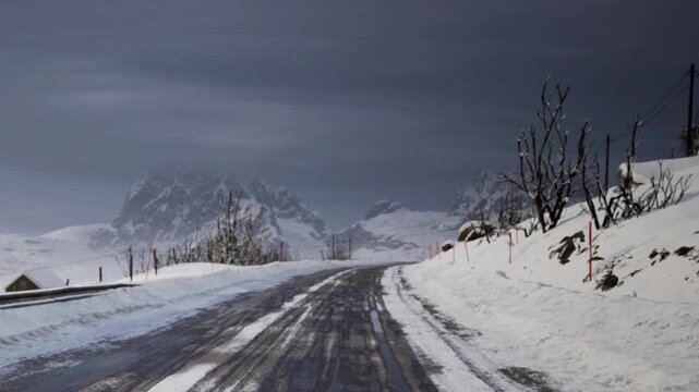 A road covered in snow stretches into the distance toward mountains under a dark sky. Few trees and power lines are visible along the route, indicating winter weather conditions.