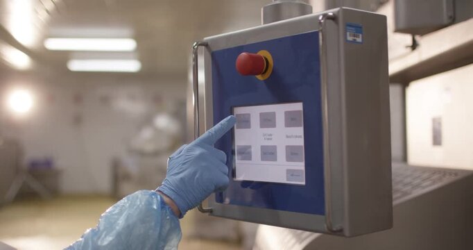 Operator touching a control panel with emergency stop button in plant