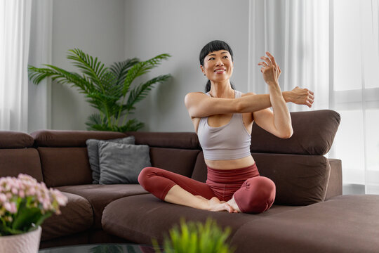 Japanese woman stretching in living room doing yoga and home workout on sofa