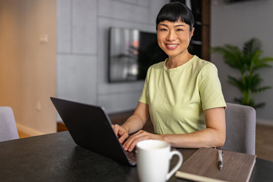 Japanese woman working on laptop at home smiling while telecommuting in modern living room