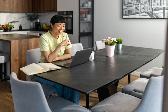 Japanese woman working from home at dining table with laptop and notebook