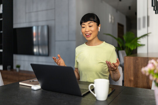 Japanese woman using laptop for a video call at home, smiling and engaged