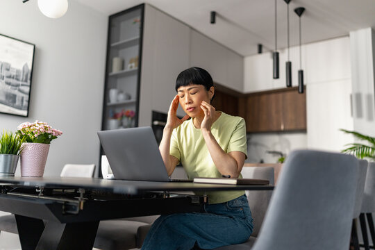 Japanese woman working from home on laptop rubbing temples and looking stressed