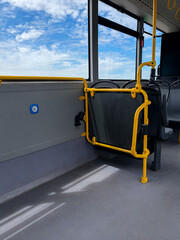 Accessible public bus interior with wheelchair space yellow safety rails and blue sky view © Daria