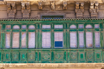 A weathered green wooden enclosed balcony with arched windows and blinds decorates a historic facade in Valletta, Malta © Tony Blood