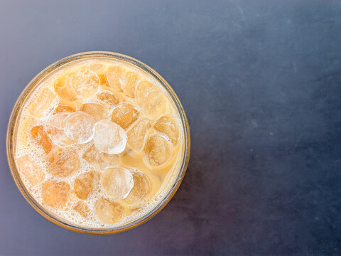 Overhead close-up of iced coffee filled with ice cubes on a dark table with simple negative space.