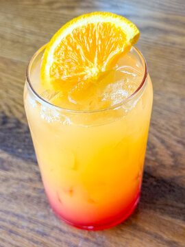 Close-up view of a bright orange iced drink with citrus garnish and red syrup layered at the bottom.