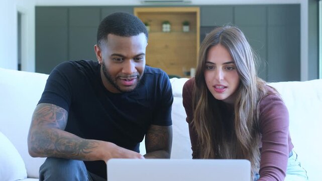 A happy couple on a sofa looks at a laptop, then excitedly celebrate their success with high-fives and cheers, laughing and hugging in joy.