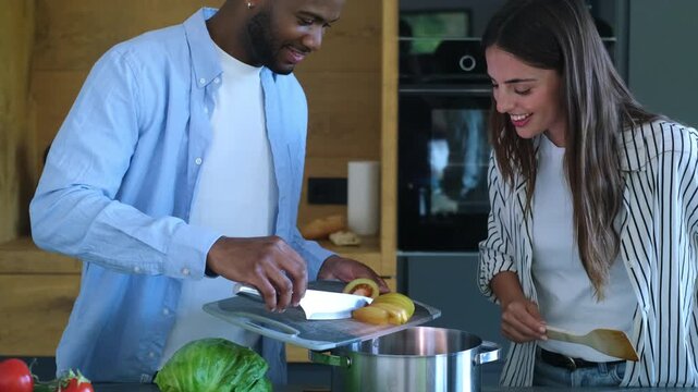 A happy mixed-race couple enjoys cooking together in their modern kitchen, preparing a healthy meal with fresh ingredients.