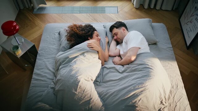 Couple embracing in bed morning sunlight. Man woman resting together bedroom