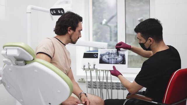 Dentist points to specific areas of the jaw on an X-ray while discussing the patient&rsquo;s dental condition and further treatment.