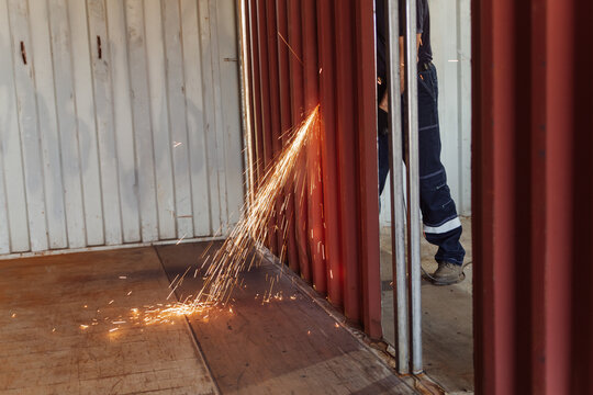 Worker using circular saw on shipping container wall