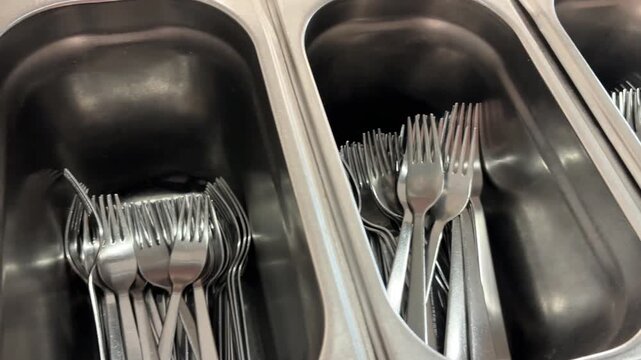 Stainless steel cutlery containers with forks and knives in a restaurant, cafeteria or commercial kitchen self-service area