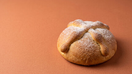 Fototapeta premium Pan de muerto bread sprinkled with sugar on a warm colored background