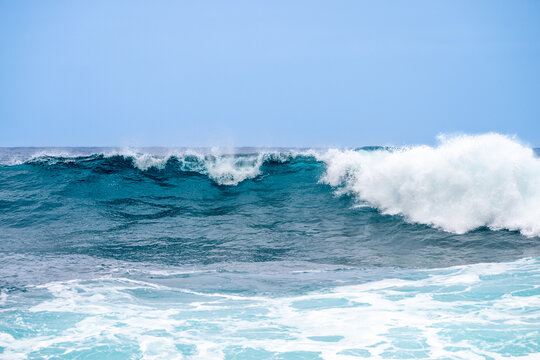Powerful blue ocean wave breaking under clear sky