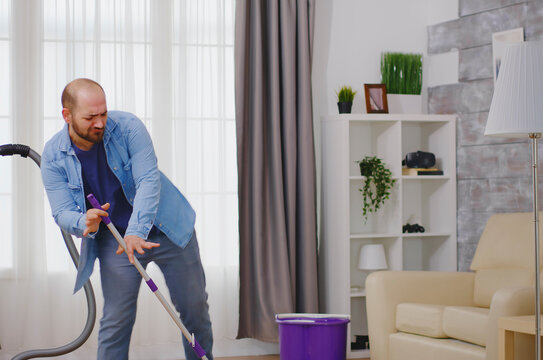 Man dances while cleaning the floor, turning apartment housekeeping into a cheerful domestic routine with vacuum or mop work and practical floor care.
