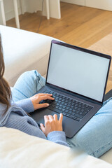 Fototapeta premium Woman working on laptop at home on a sofa, typing with casual jeans and blue sweater, remote work and online study in a cozy modern living room workspace