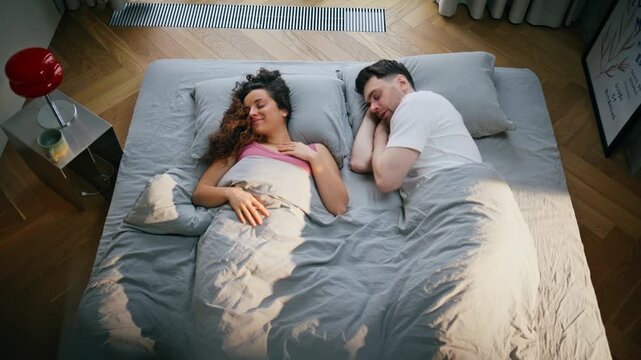 Couple sleeping bed morning together. Man woman cuddling under blanket bedroom.