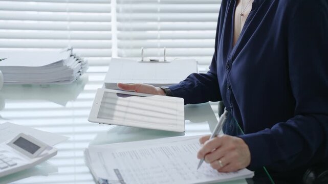 Professional woman using digital tablet for business tasks, typing data and reviewing documents at a modern office desk, symbolizing efficiency and financial management