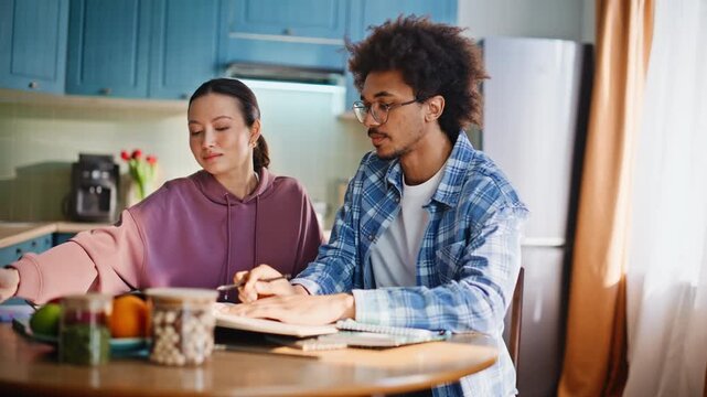 Multiethnic couple studying together at kitchen table. Students doing homework