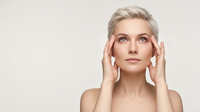 Flawless skin care model with natural makeup and a platinum pixie cut touching her temples. Minimalist composition with a 16:9 aspect ratio and ample copy space.