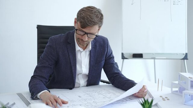 Architect in glasses working on blueprints and architectural model, planning a new building project, designing innovative construction solutions in a modern office
