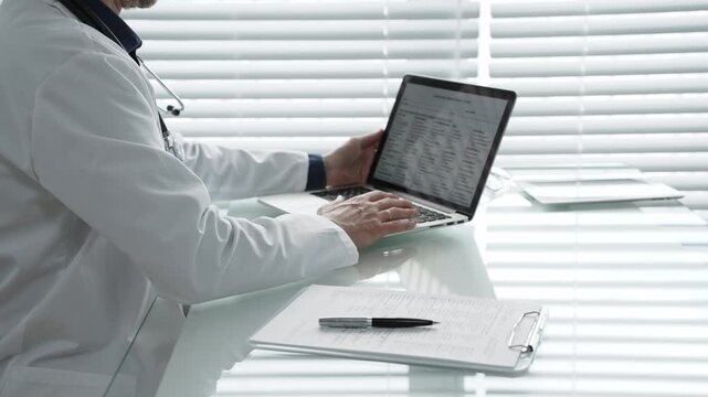 Doctor sitting at a desk, typing on a laptop with a stethoscope around their neck, reviewing patient data and managing electronic health records during a work day
