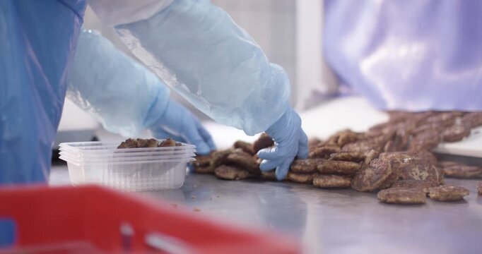 Gloved hands pack fried patties into plastic trays