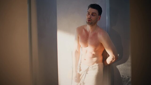 Muscular wet man wrapping towel around waist. Male portrait steamy bathroom