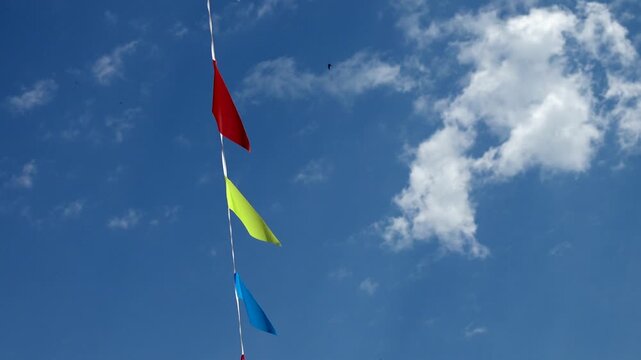 Colorful prayer flags flutter against a bright blue sky  .Tibetan prayer flags in vibrant colors are strung together and blowing in the wind against a clear blue sky with fluffy white clouds