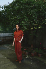 Obraz premium Vibrant lifestyle moment with a woman in a red dress outdoors, relaxed pose, soft smile, sunlit scene, leafy background, natural colors, casual elegance