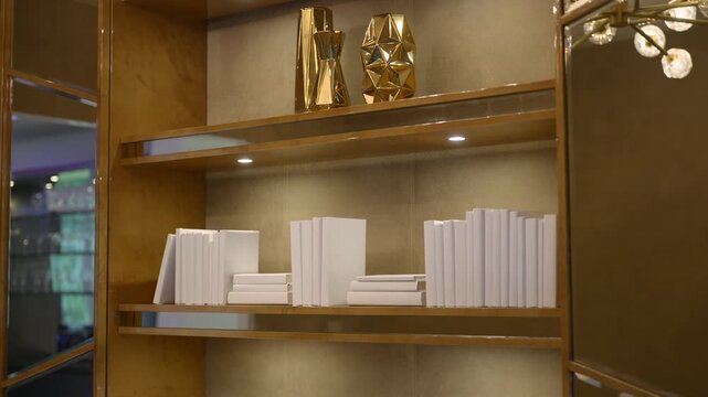 Bookshelf looks clean and cozy with white books and warm light. Gold wall adds soft glow. Simple lines and calm tones make space feel fresh and modern
