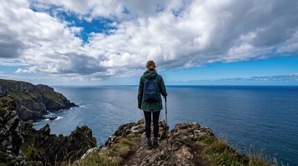 Fototapeta premium Young woman hiker standing on a rocky cliff edge overlooking the vast ocean, representing freedom, adventure, travel, solitude, and personal exploration goals