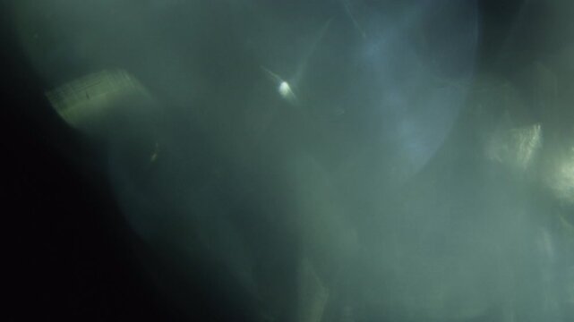Abstract ethereal light flares moving across a dark mysterious background.