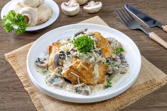 Chicken thighs with creamy mushroom and cheese sauce on a wooden table.