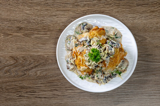 Chicken thighs with creamy mushroom and cheese sauce on a wooden table.