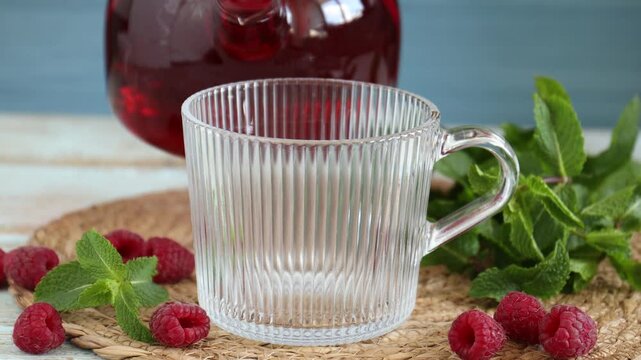 Woman pouring aromatic raspberry tea into glass cup at wooden table, closeup