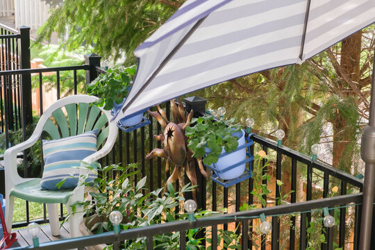 Cozy home balcony terrace with green chair, striped umbrella, potted plants and decorative sun