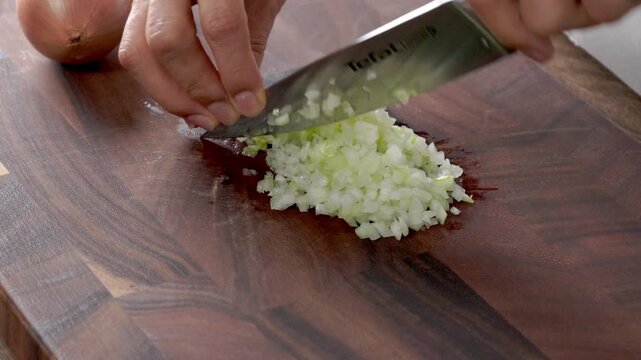 A woman is preparing food in her home kitchen. She is chopping onions with a knife on a cutting board.