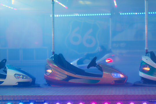 Empty bumper cars at amusement park with colorful lights and foggy atmosphere