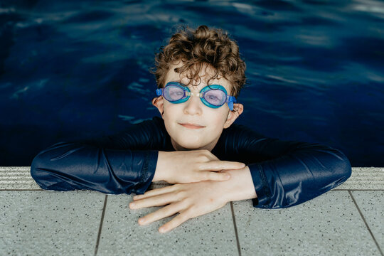 Portrait of a happy young boy wearing swimming goggles learning to swim in an indoor swimming pool
