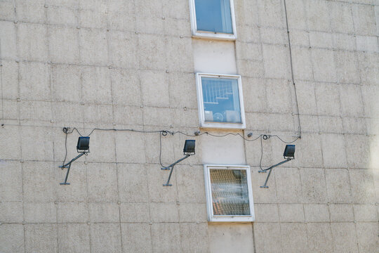 Exterior view of a textured concrete building wall with three windows and mounted floodlights