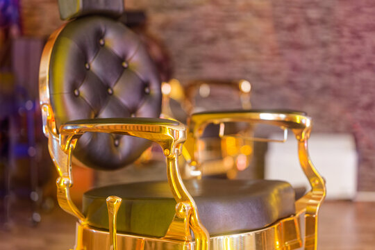 Luxurious vintage barber chair with black leather and golden metal frame in salon interior