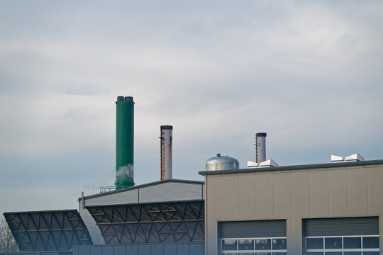 Industrial factory buildings with chimneys emitting smoke under cloudy sky