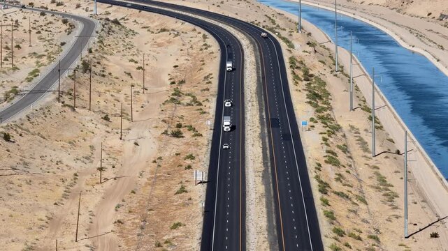 Highway running parallel to a long water canal through a dry sandy landscape, high-angle aerial view