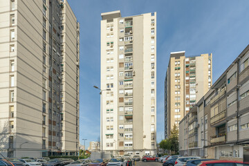 Tall residential apartment buildings towering over a crowded parking lot filled with cars under a clear blue sky. © Toyakisfoto.photos