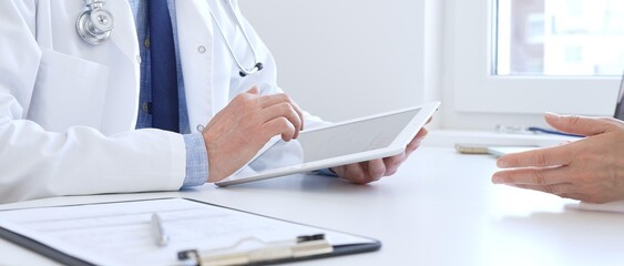 Fototapeta premium Close-up of doctor man showing information on tablet to patient woman during medical visit, explaining diagnosis and treatment options, providing medical consultation. Medicine concept