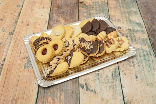 Variety of shortbread biscuits including chocolate-dipped, nut-topped, and jam-filled cookies arranged on a silver tray on wood.